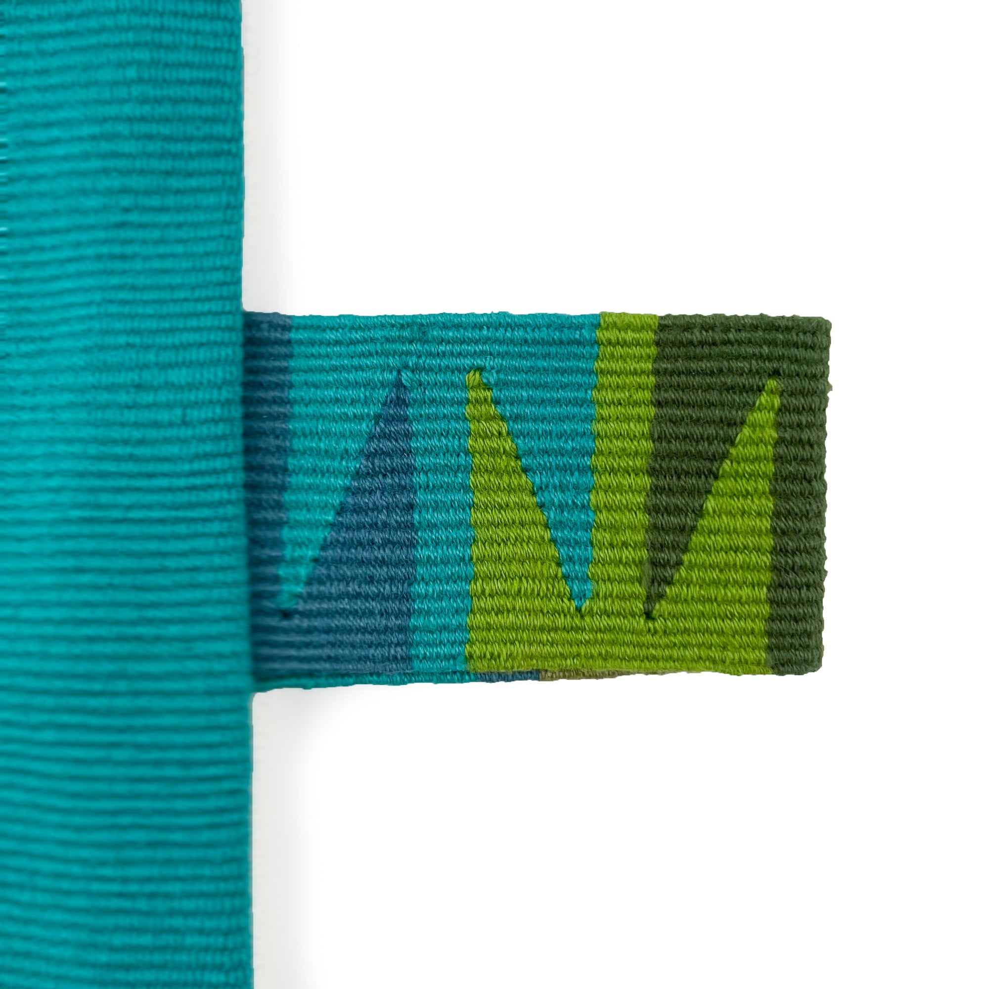 Front of rectangular cushion with color block panels in turquoise, green with black and white randa detail, and teal, with colorful cinta tag