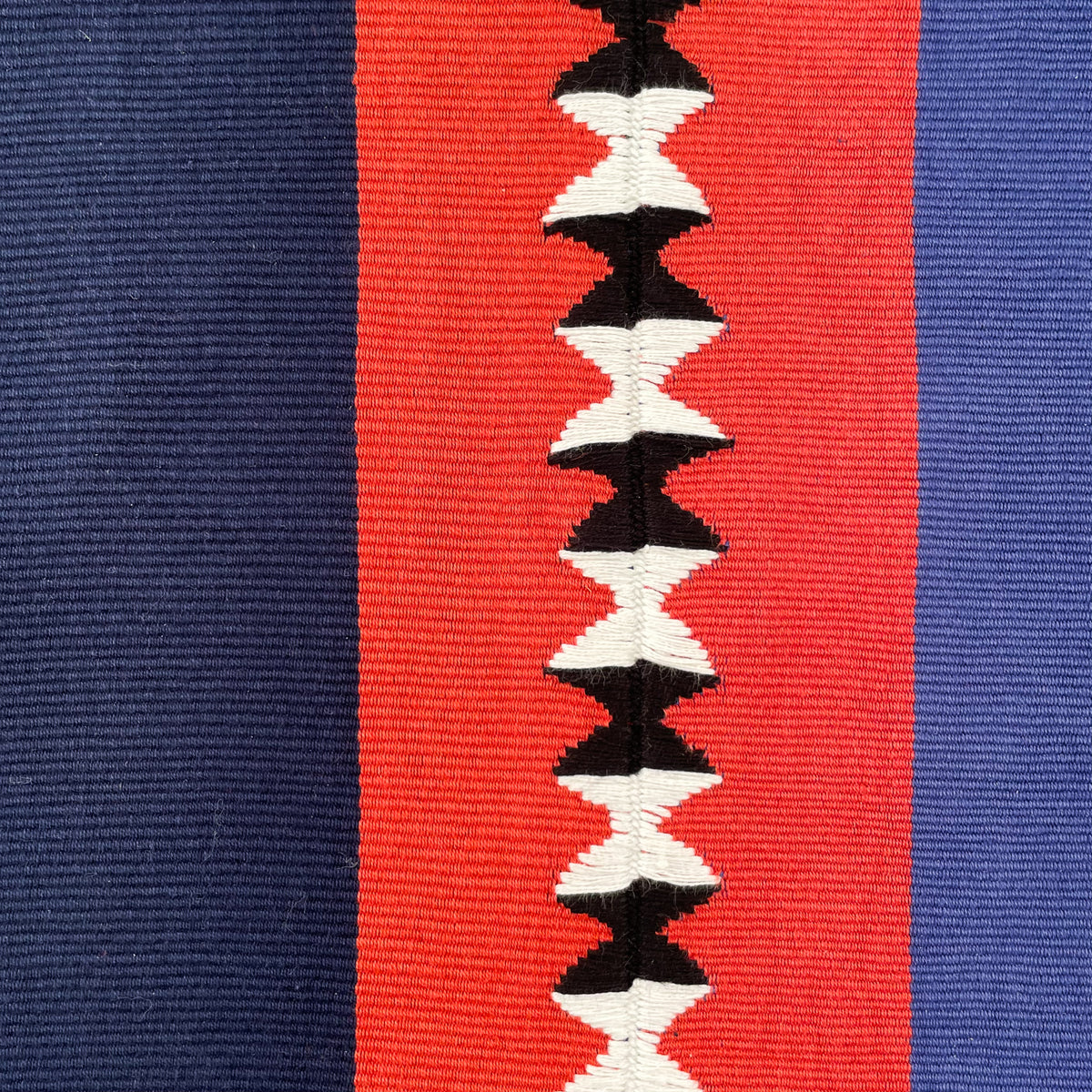 Close up swatch of cushion cover with color block panels in navy, red with black and white randa detail, and purple