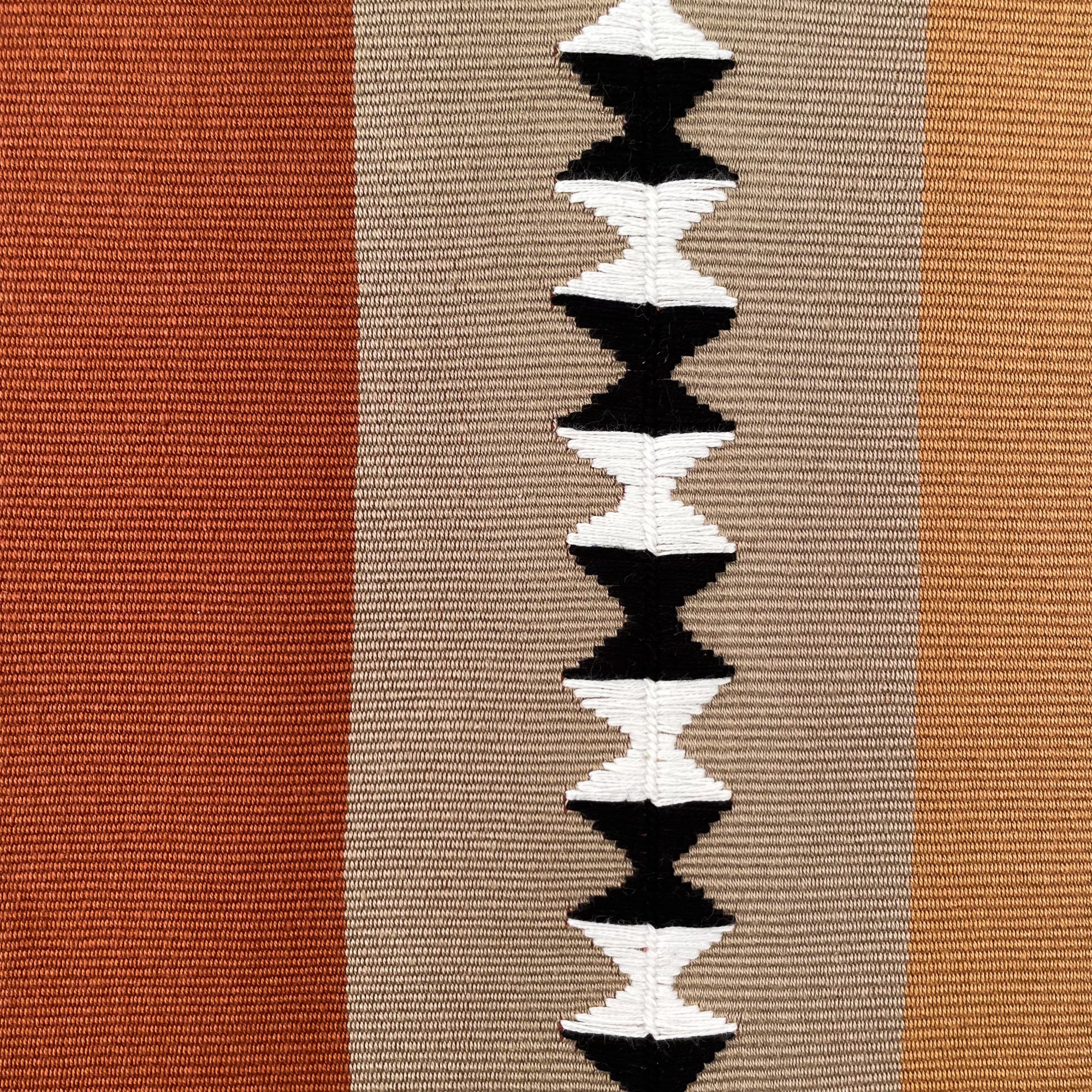 Front of rectangular cushion with color block panels in different shades of brown, with black and white randa detail on center panel, with colorful cinta tag