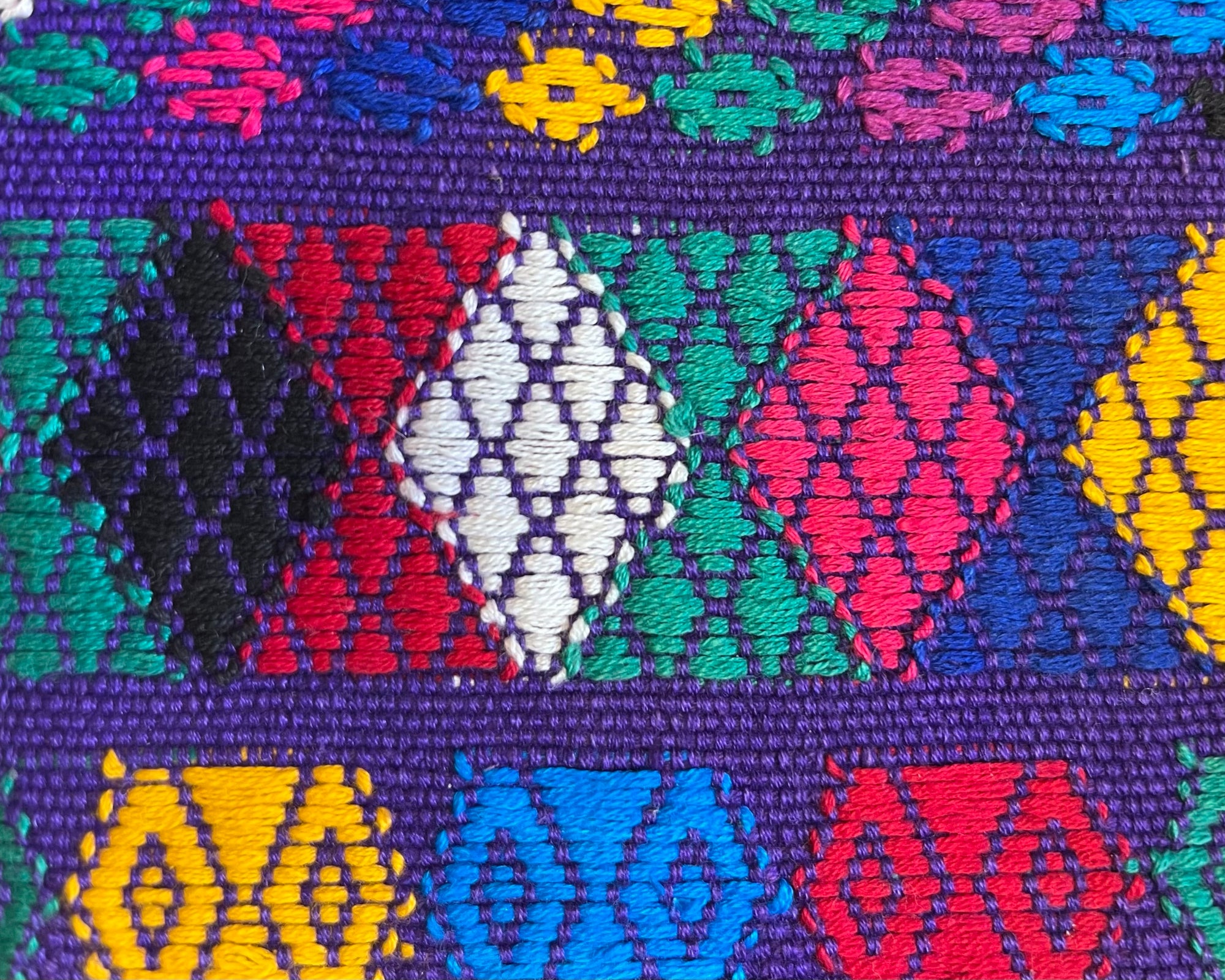 Close-up image of a purple handwoven textile from San Rafael, Rabinal, Guatemala with bright multicolored geometric brocade designs