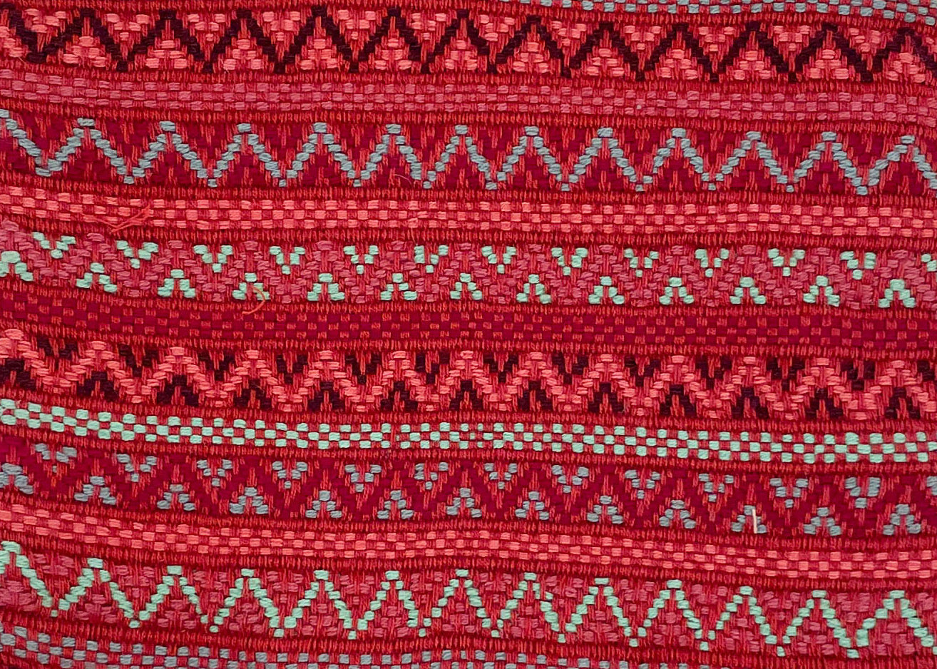 Close-up image of red handwoven brocade textile with intricate, dense brocade geometric designs