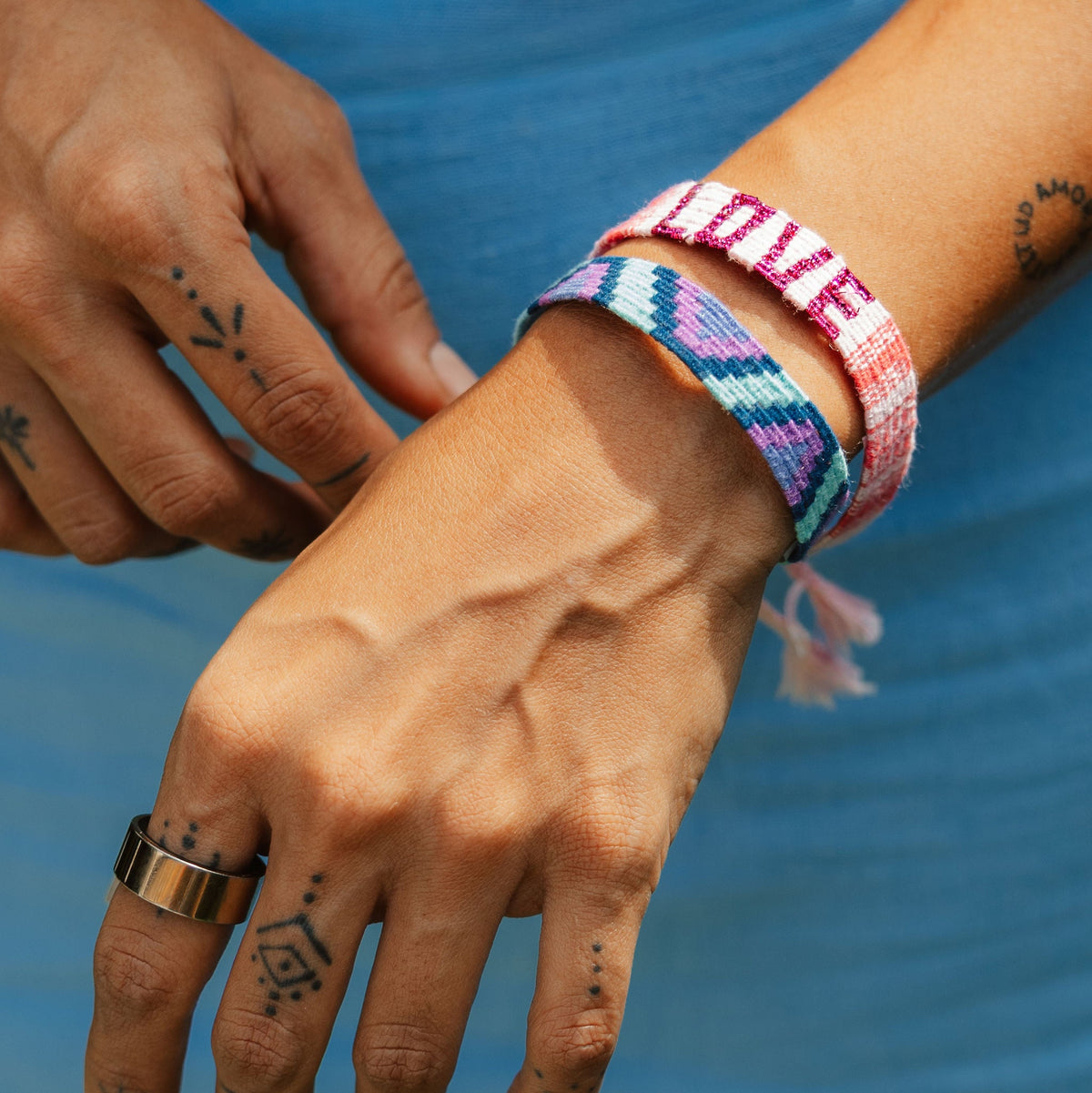 Closeup of Love Sparkle Bracelet in Pink and another bracelet on person's wrist, with opposite hand in background.