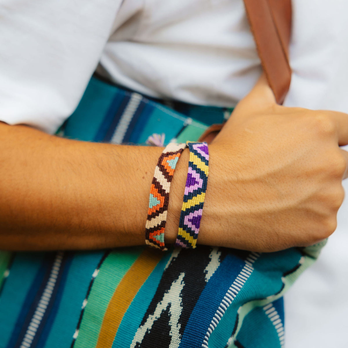Closeup of Marta bracelets in Terracotta and Lime&Purple being worn on person's wrist, with striped back in background.