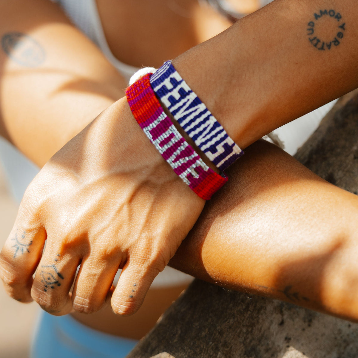 Closeup of Feminist Bracelet and Sparkle Love Bracelet in Red on person's wrist, and with opposite arm in background.