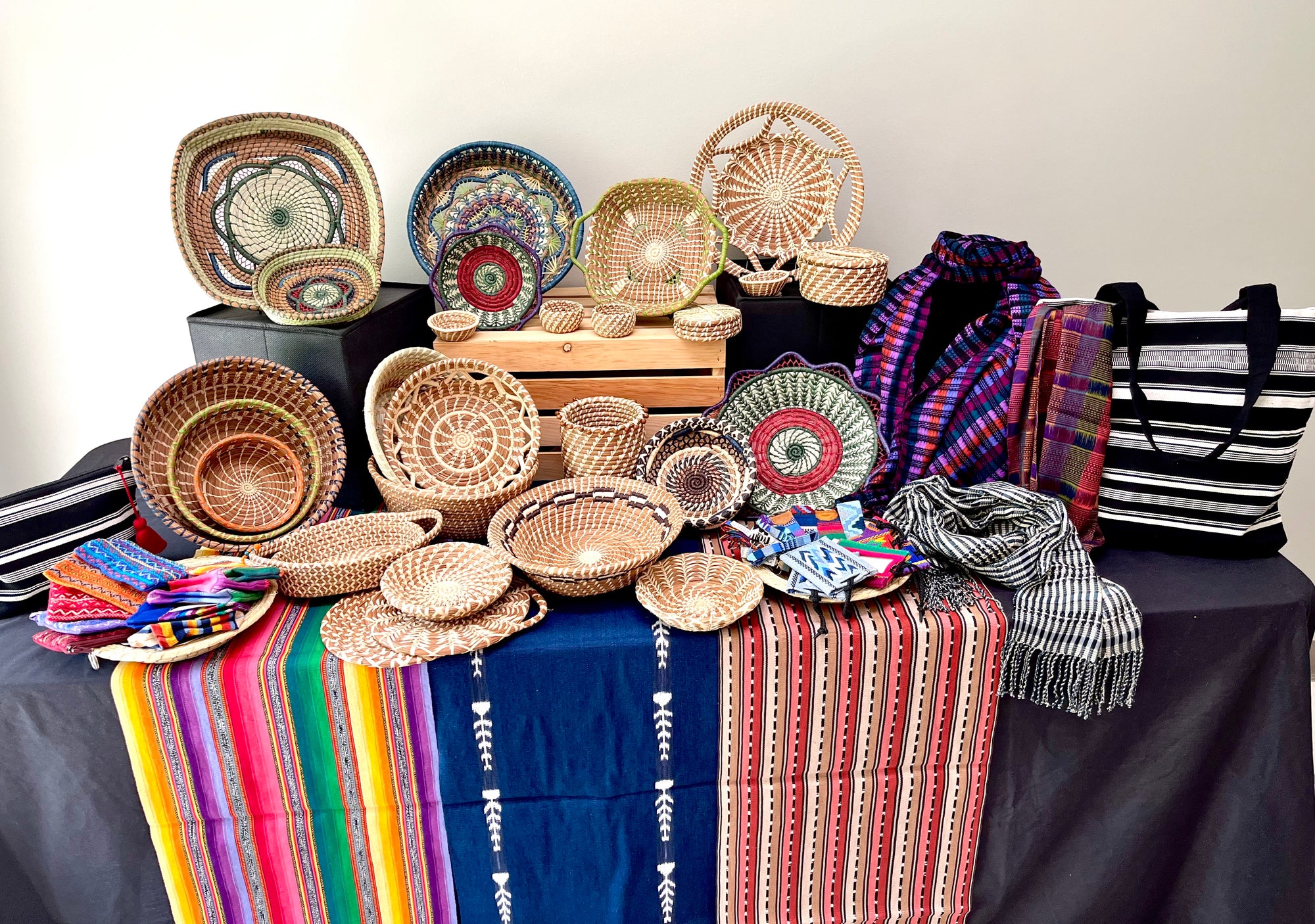 A beautiful assortment of handwoven table linens, pine needle baskets, and colorful scarves arranged in a tabletop display