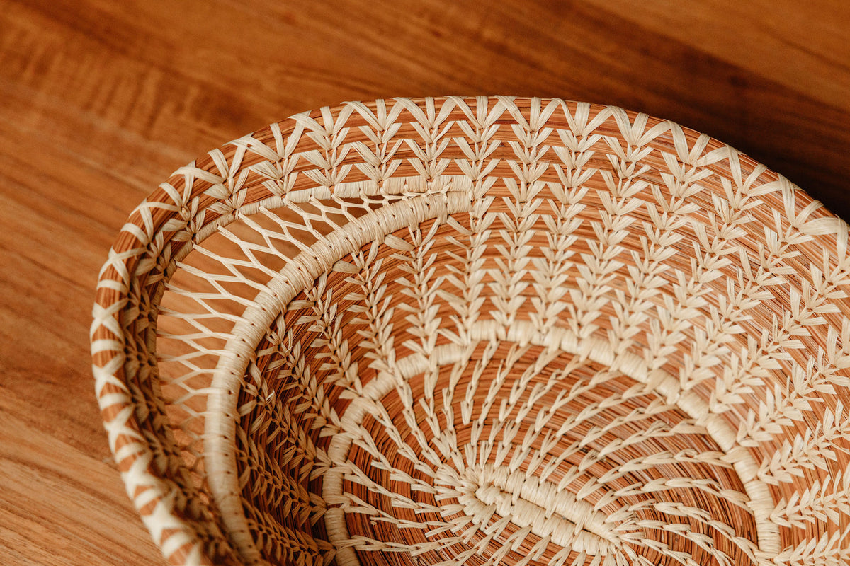 Close up of the Haida Basket, showing intricate raffia stitching and mesh detail on the basket handle, with wooden table background.