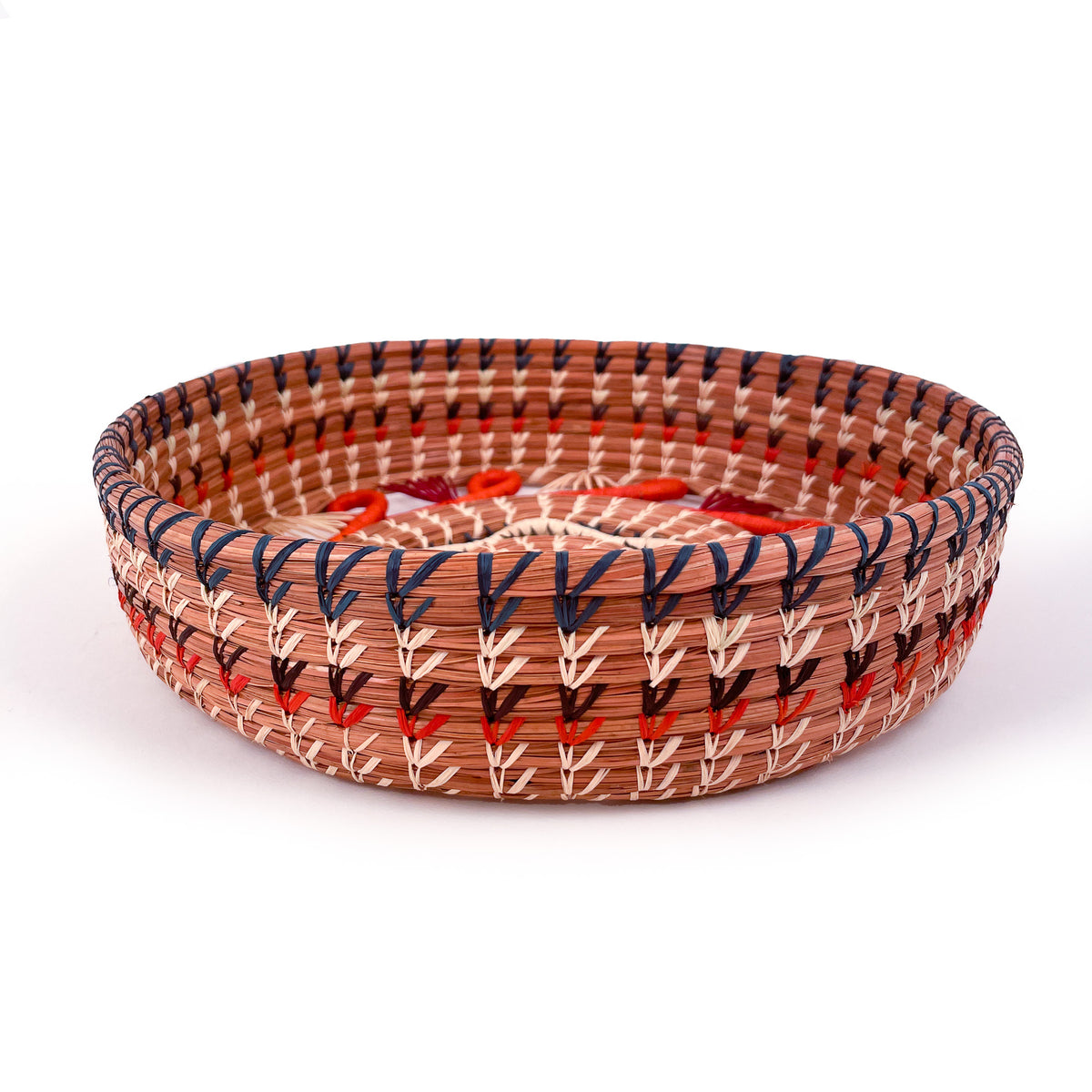 Side view of Cristina basket, showing raffia stitching in blue, natural, brown, and orange on natural pine needles