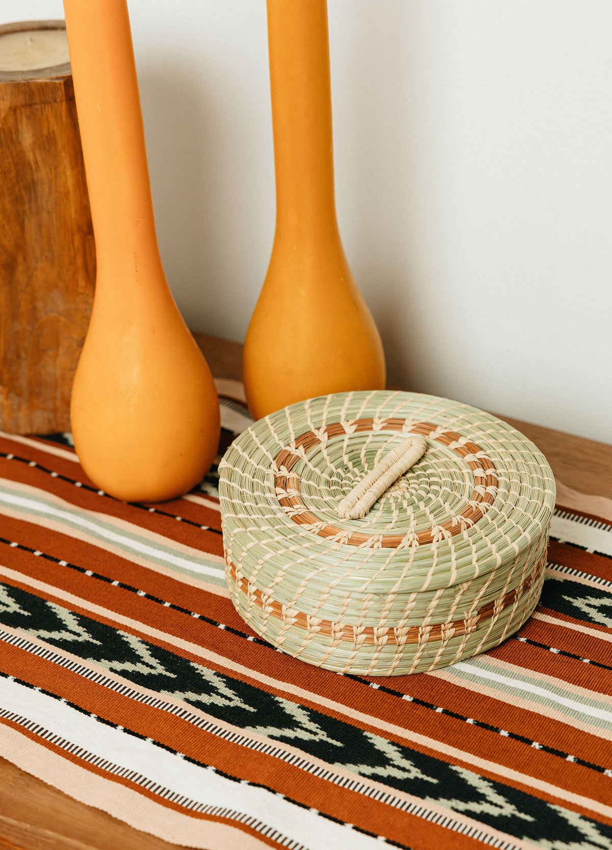 A tortilla basket handwoven from grass sits on a table runner with chevron pattern, with candle holders in the background.