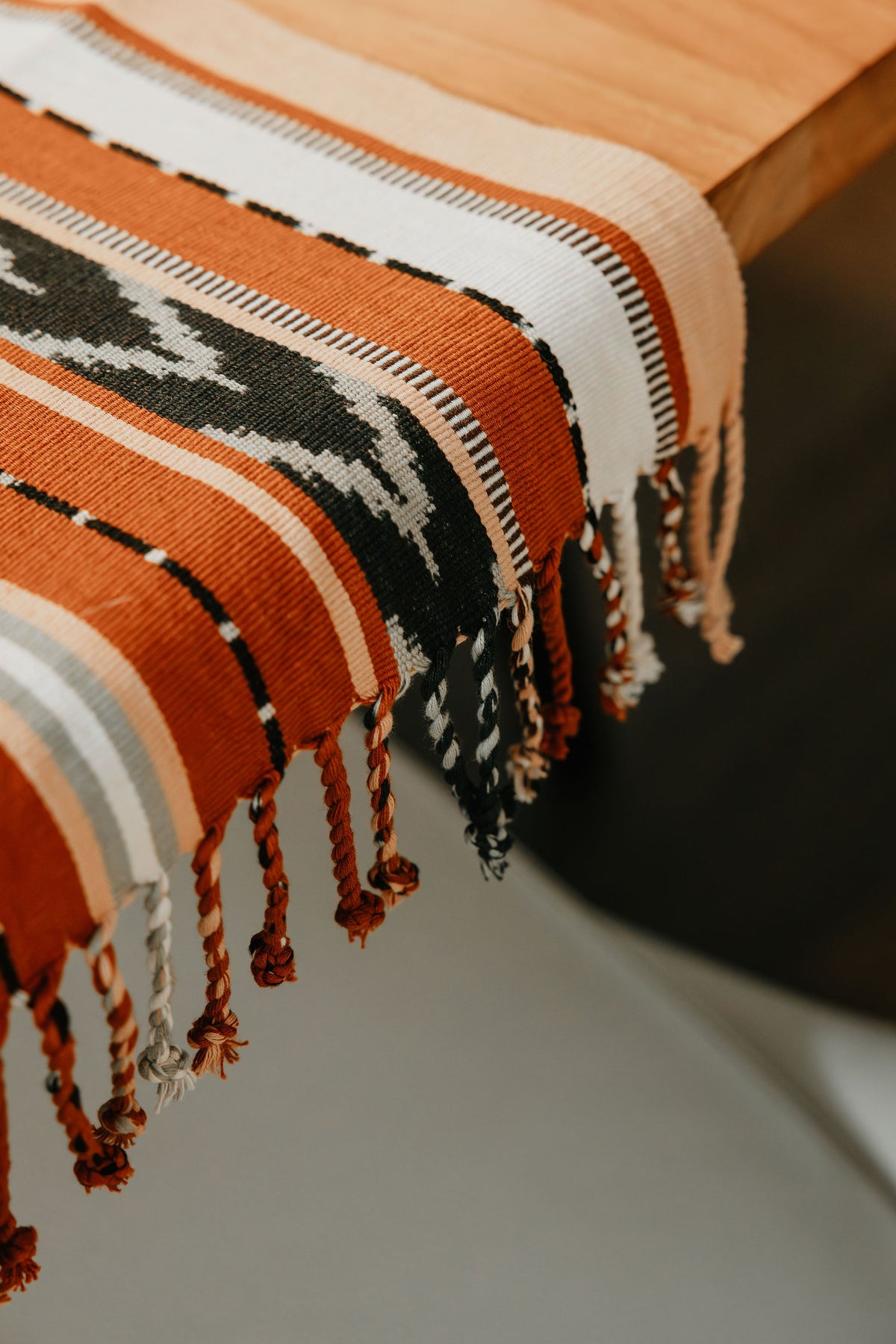 Closeup of the Flecha Jaspe Table Runner draped over the end of a table, showing the chevron jaspe and fringe details.