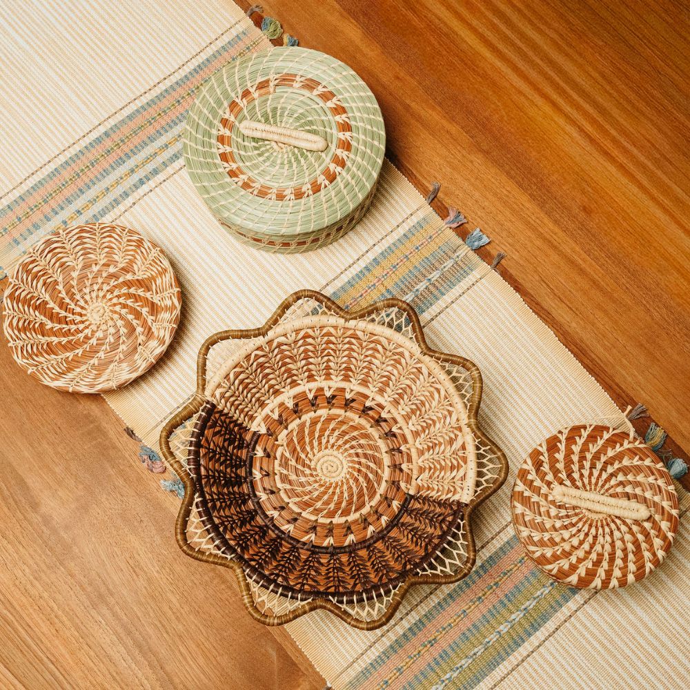 A woven textile ttable runner in beige with textured stripes in blue, yellow, and pink, finished with intricate mesh tassels on a white background.