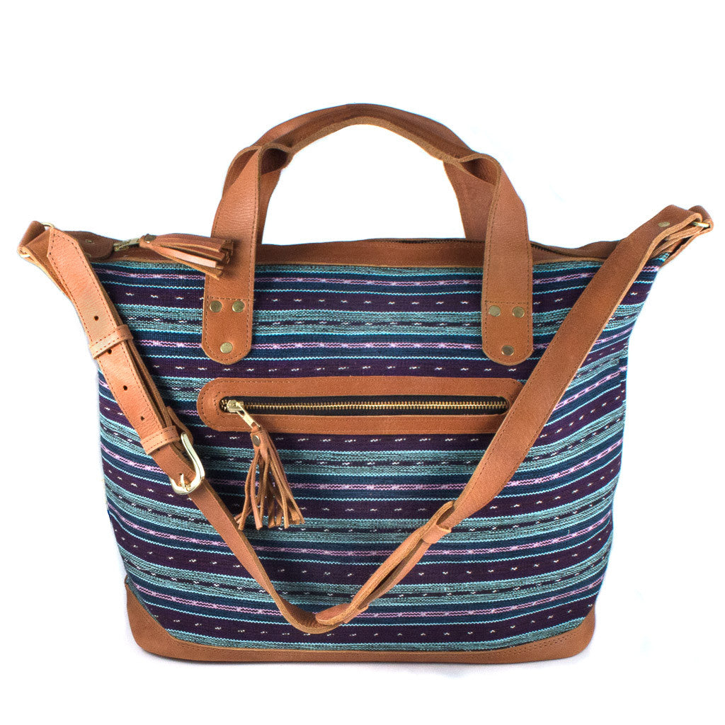 Large weekender travel bag with horizontal striped pattern in blue, purple, and pink.  Bag has leather shoulder strap, handles, zipper trim, and bottom.