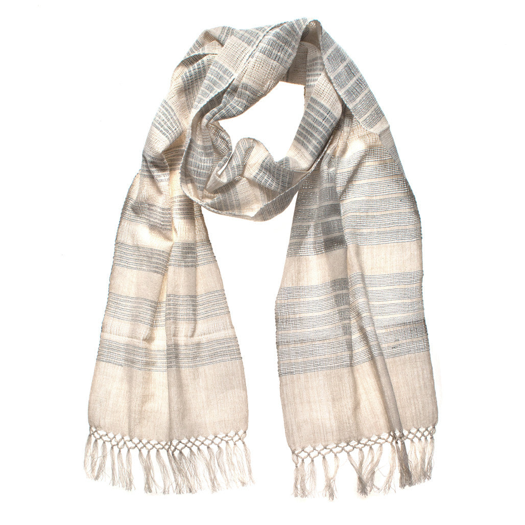 Recycled Thread Scarf, a gauzy weave made from recycled cotton and denim threads, with alternating stripes of natural cotton and denim of different widths, with fringe. The scarf is laid flat, wrapped with a circle on white background.