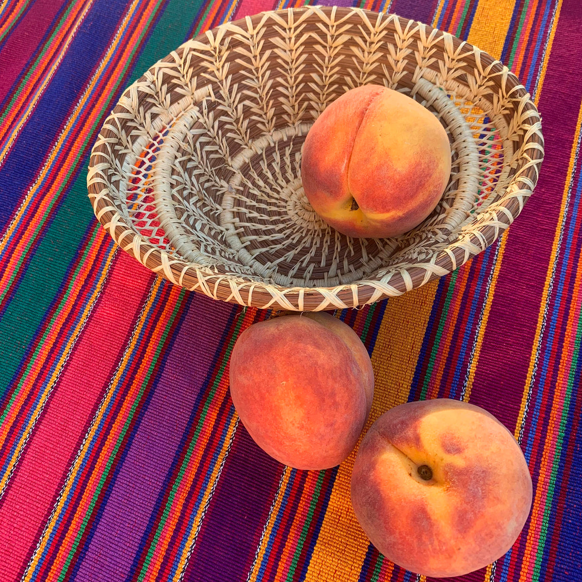 peaches and pine needle basket on handwoven tablecloth
